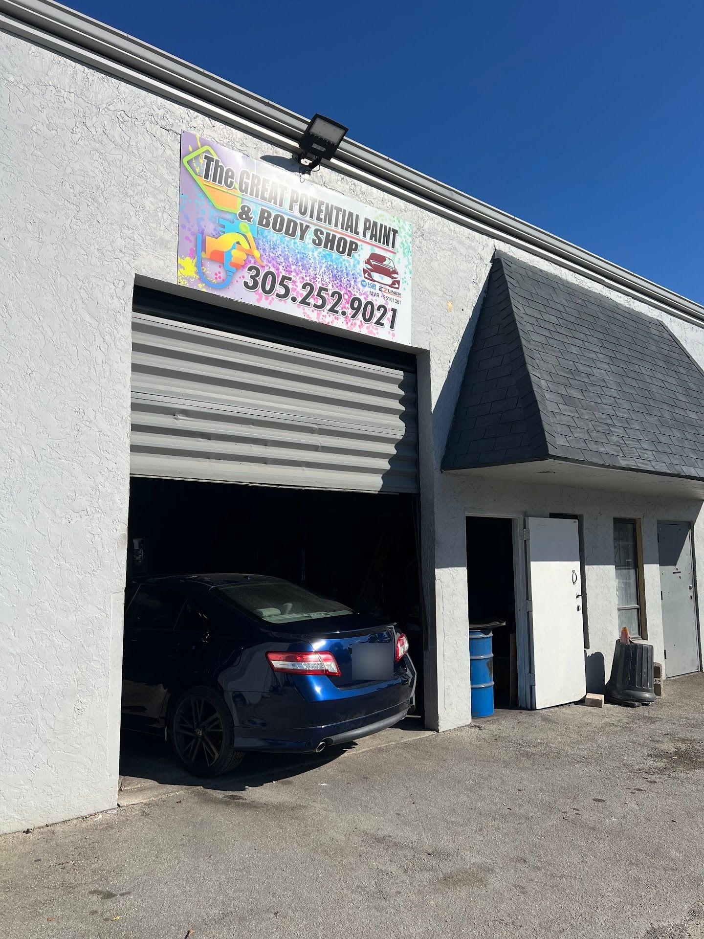 The shop's open bay door with a blue sedan inside, under the rainbow Great Potential sign
