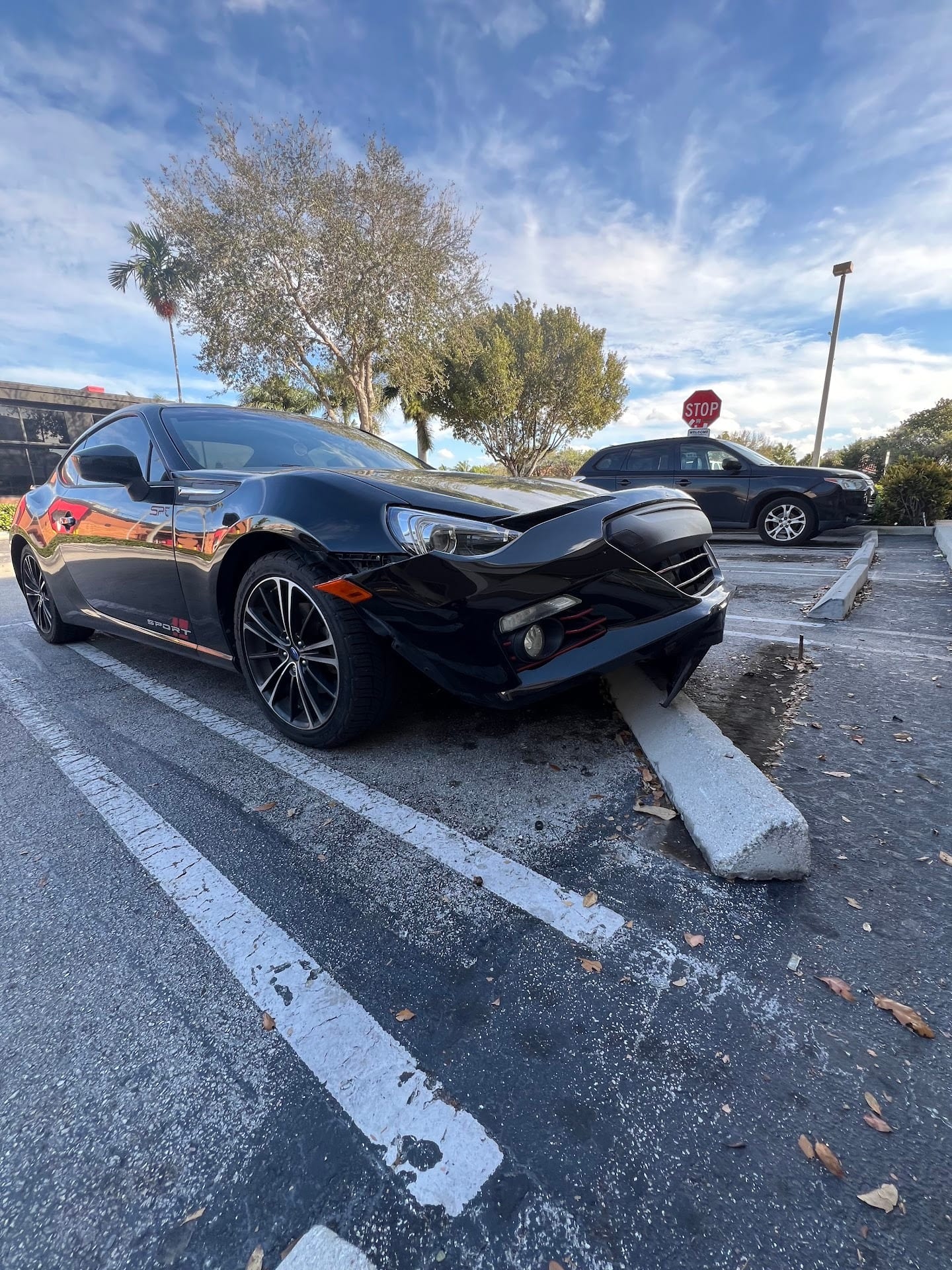 Black Subaru BRZ with its front bumper crushed against a concrete parking stop