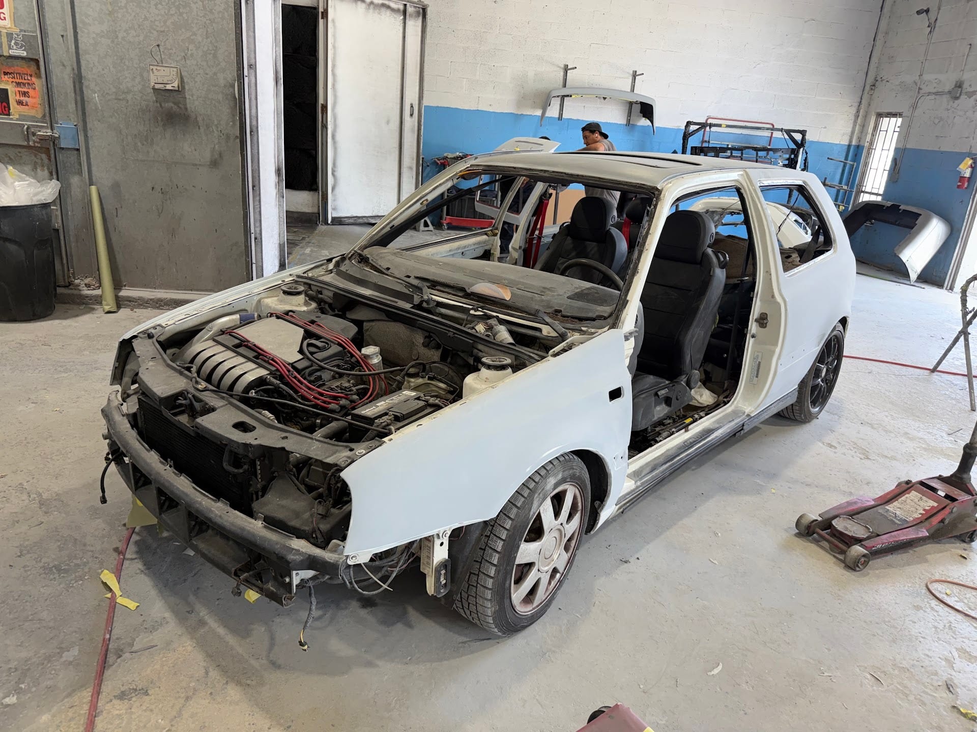 White VW Golf stripped to the shell and primed, engine bay open, in the shop
